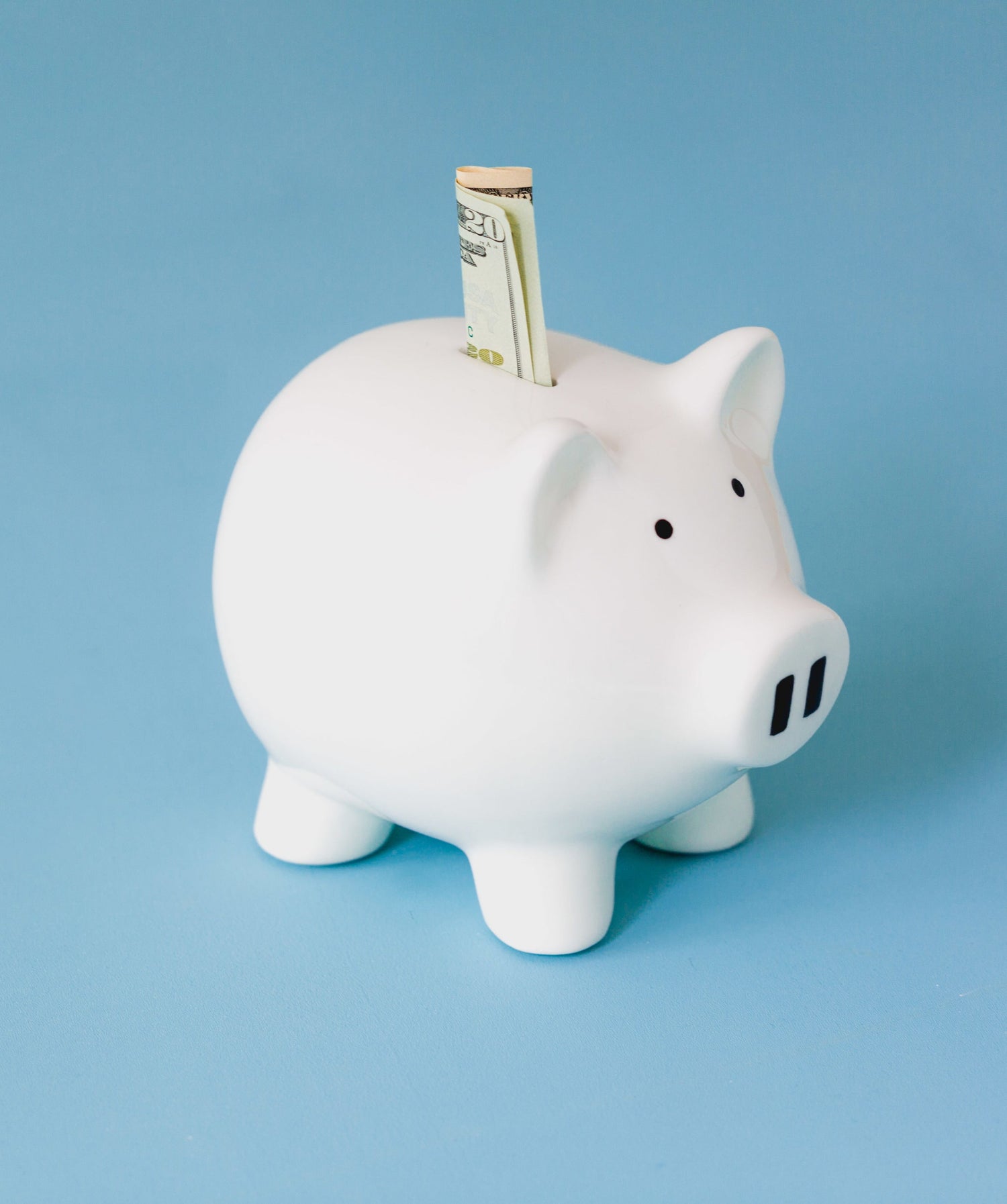 A piggy bank with a bank note half-way in, light blue background. 
